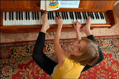 Niña tocando el piano con manos y pies.